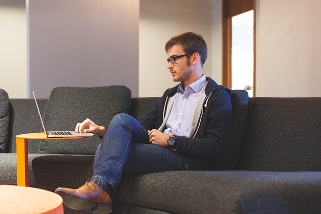 Seorang pria duduk santai di sofa sambil bekerja dengan laptop