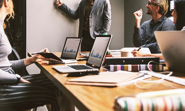 seorang karyawan yang bekerja di kantor modern dengan suasana kolaboratif, meja kerja yang rapi, dan rekan kerja yang sedang berdiskusi secara santai.